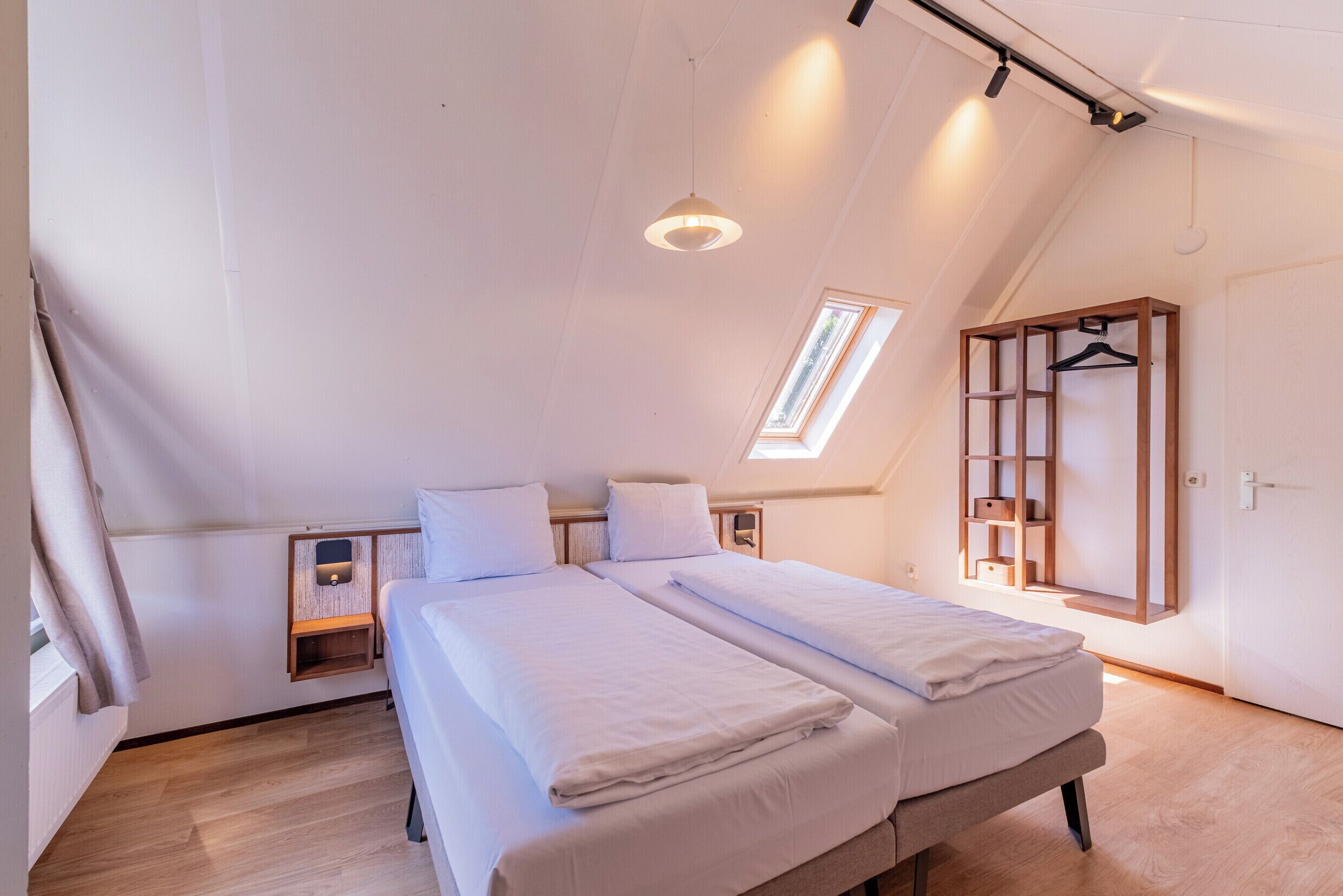 Ein Schlafzimmer mit zwei Betten, einem Dachfenster, einem Kleiderschrank und einem Nachttisch mit einer Lampe.