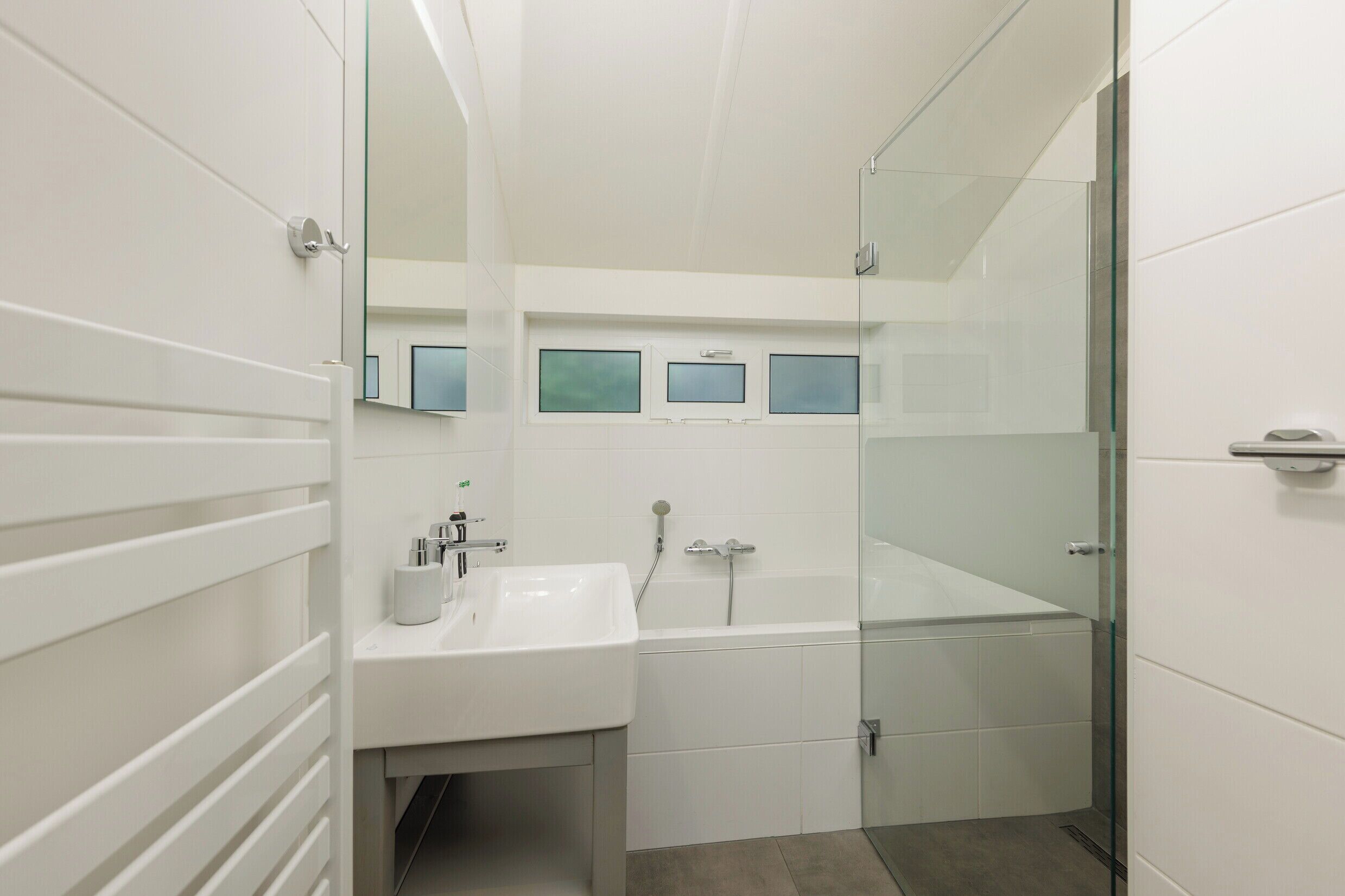 A modern bathroom with a white sink, a glass-enclosed shower, and a mirror above the sink.