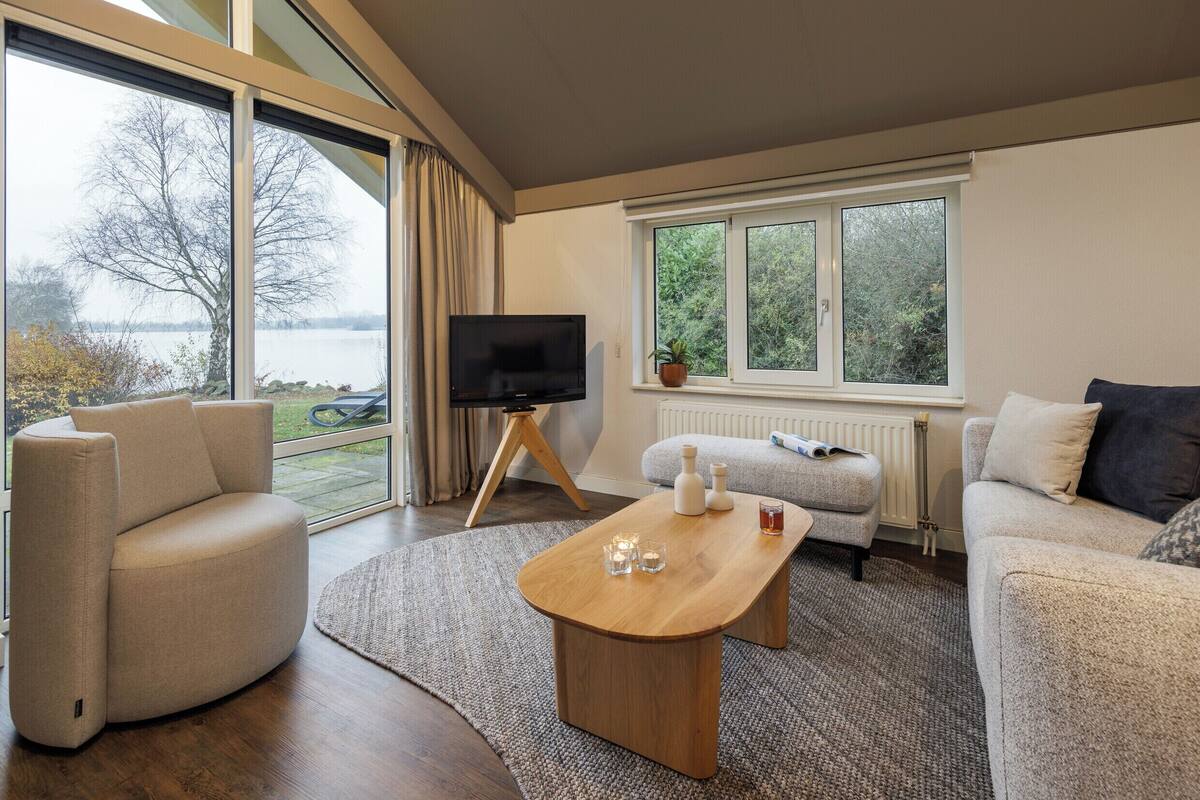 A modern living room with a large window, a flat-screen TV, a wooden coffee table, and two sofas.