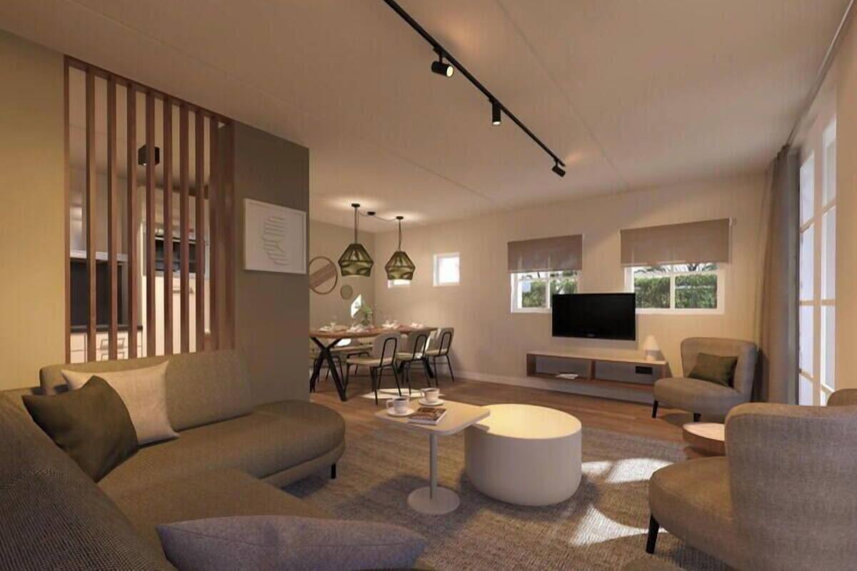 A modern living room with a sofa, coffee table, and TV. There is a dining area with chairs and a table.