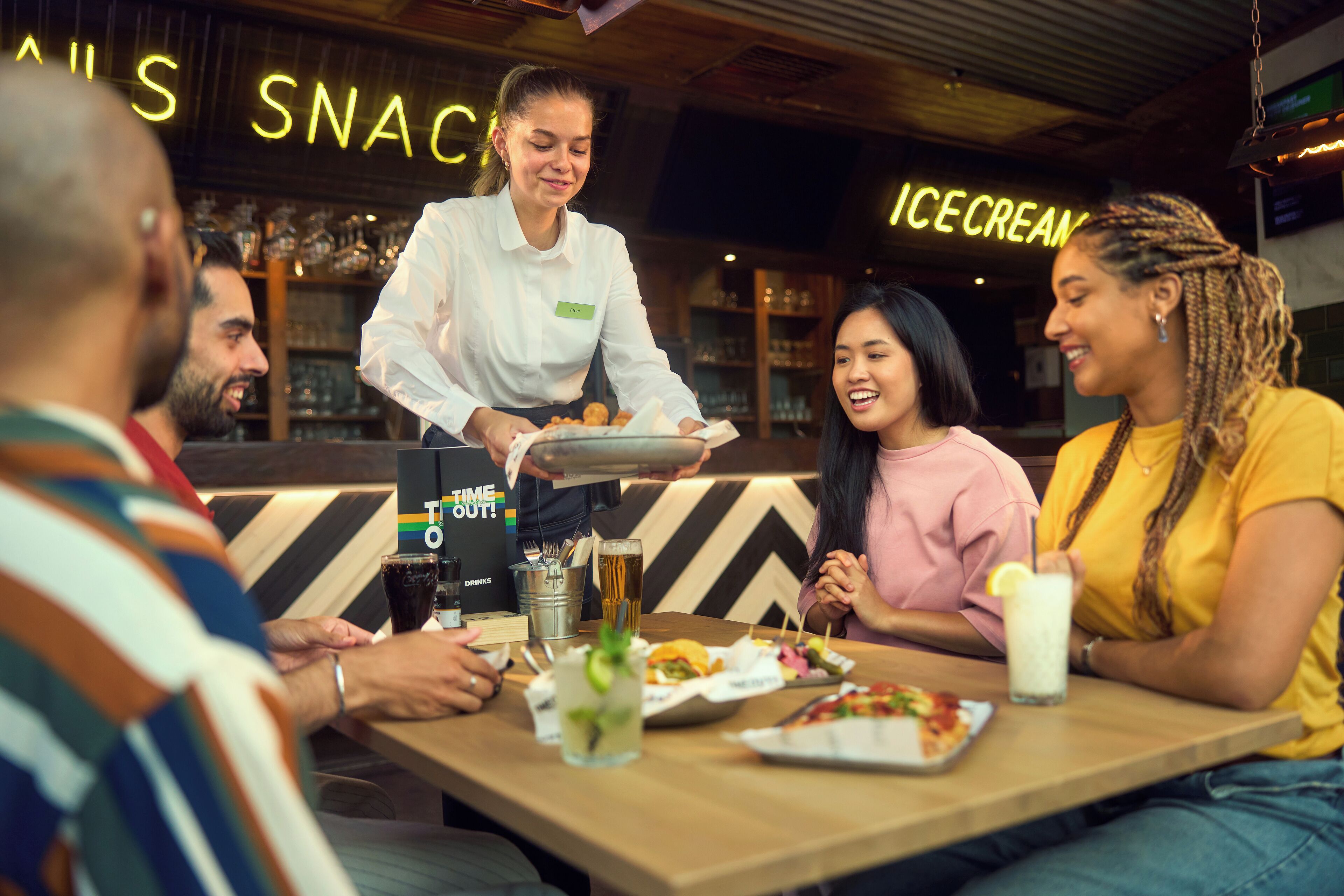Une scène de restaurant où un serveur apporte des plats aux clients assis à une table.