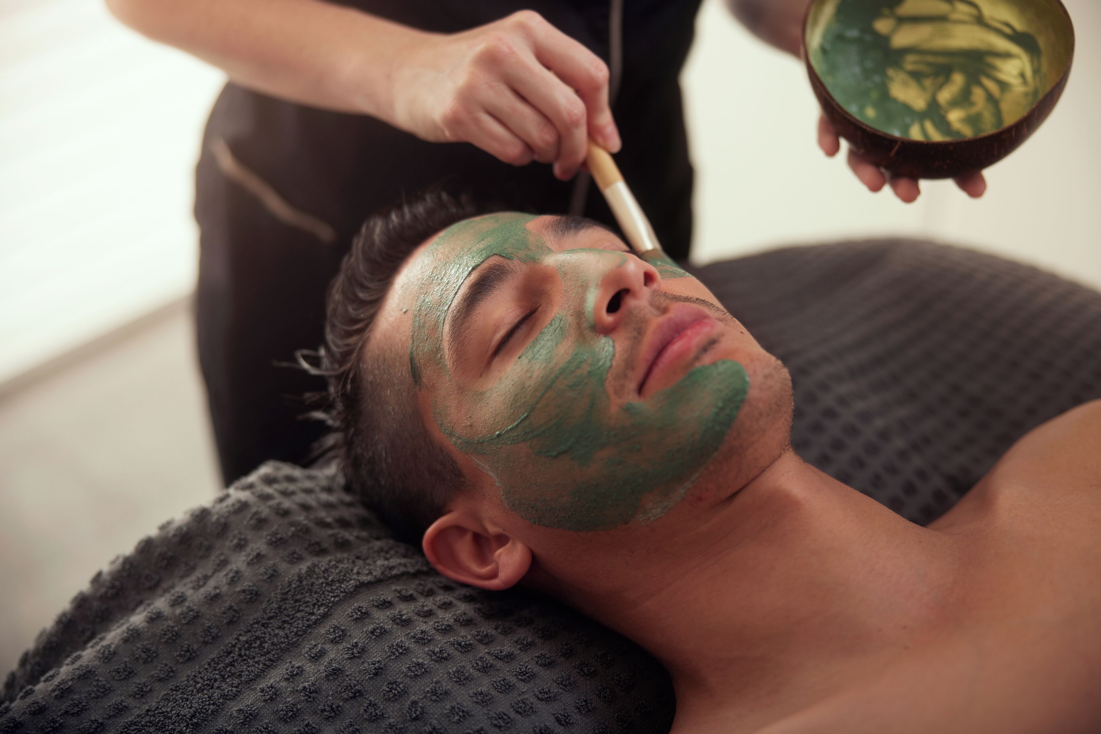 A person receiving a facial treatment with a green mask.