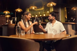 A couple at a restaurant table with a bottle of water, a glass of wine, and a plate of food.