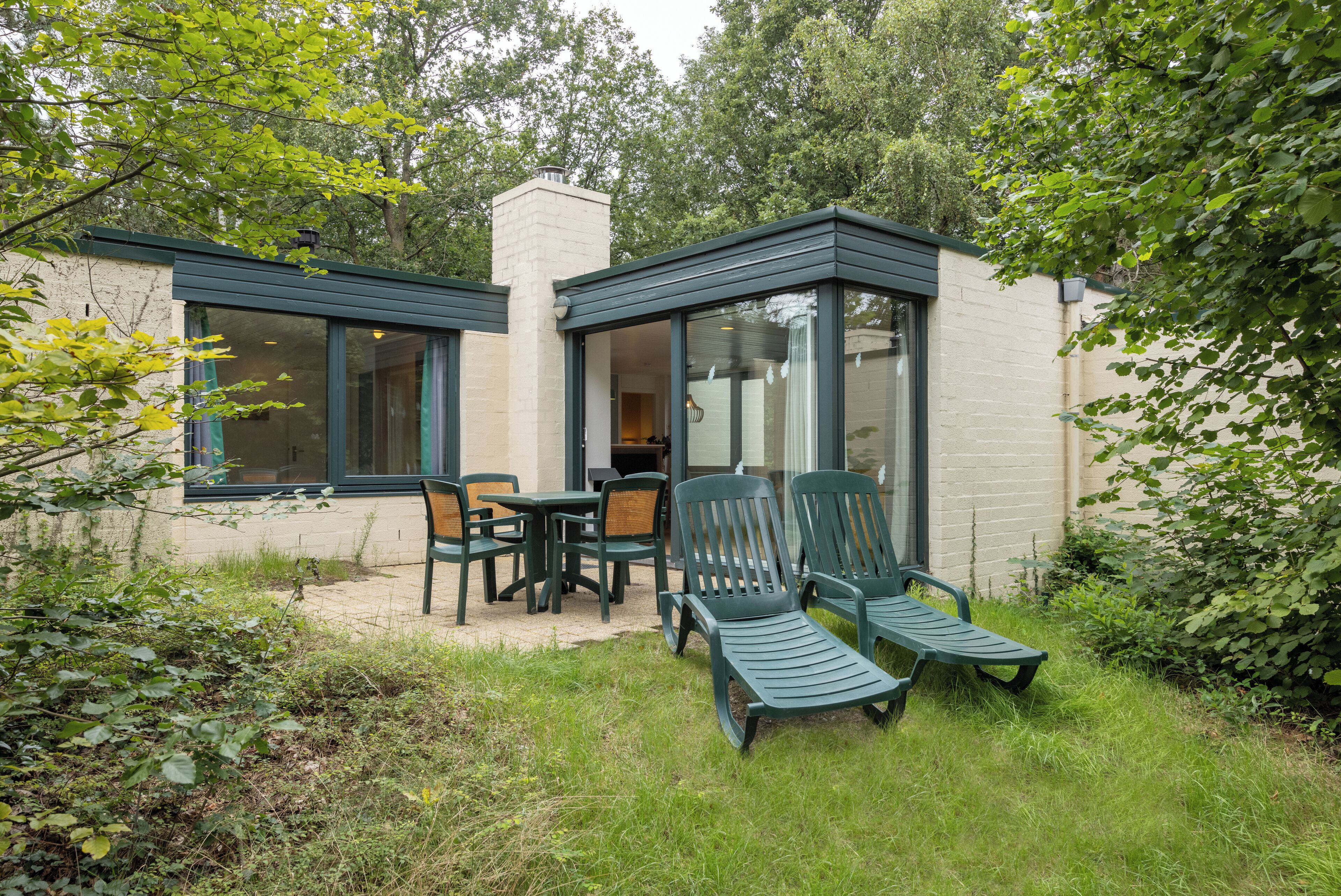 Een terras met een tafel en stoelen, omgeven door groen.