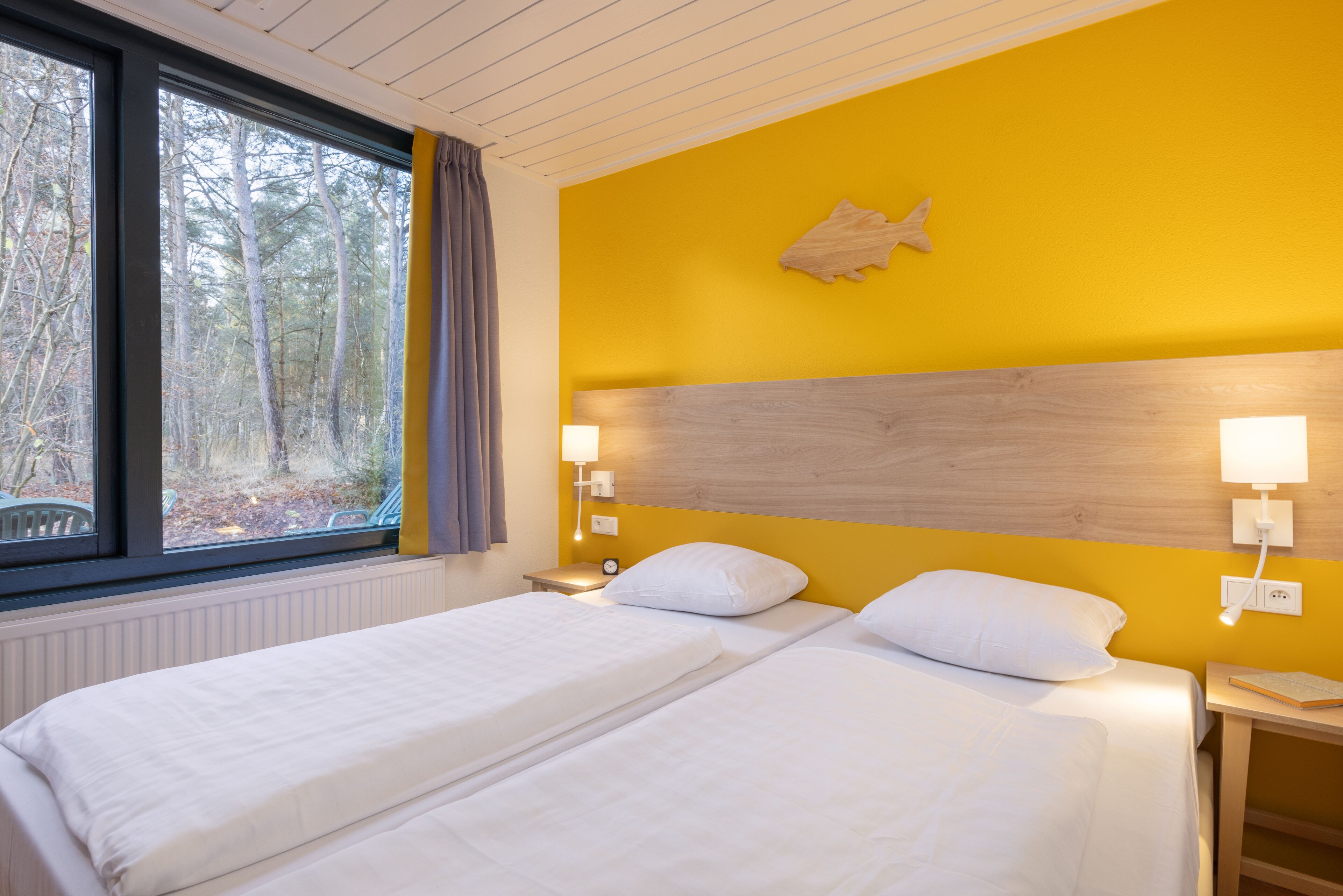 Een tweepersoonsbed met witte lakens, een houten hoofdbord en bedlampjes.