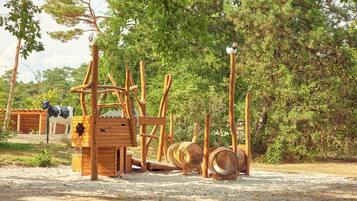 Une structure de jeu en bois rustique, dotée d’un toboggan et d’éléments d’escalade, installée dans un espace naturel et boisé.