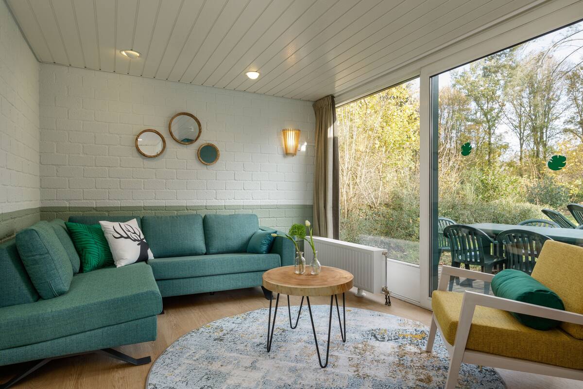 A modern living room with a green sofa, a round wooden coffee table, and a yellow armchair.