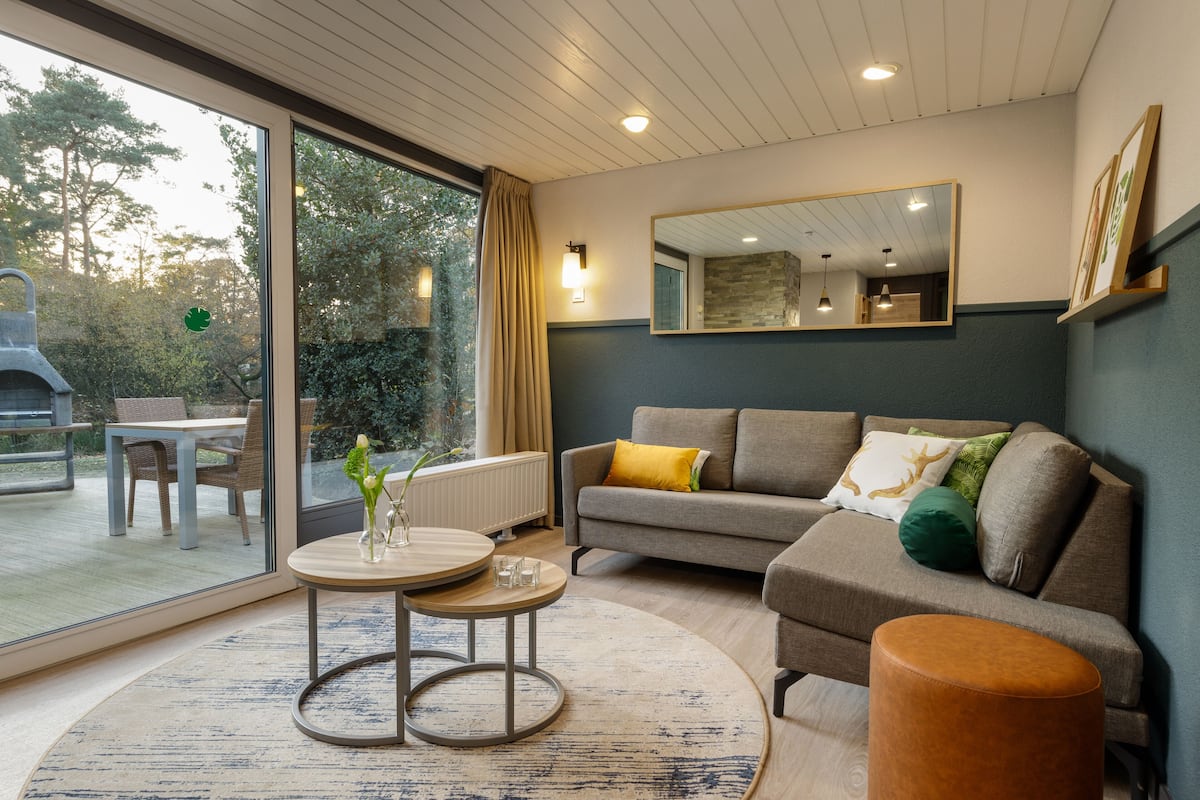A modern living room with a sofa, a coffee table, and a round table. There is a large window with a view of the outdoors.