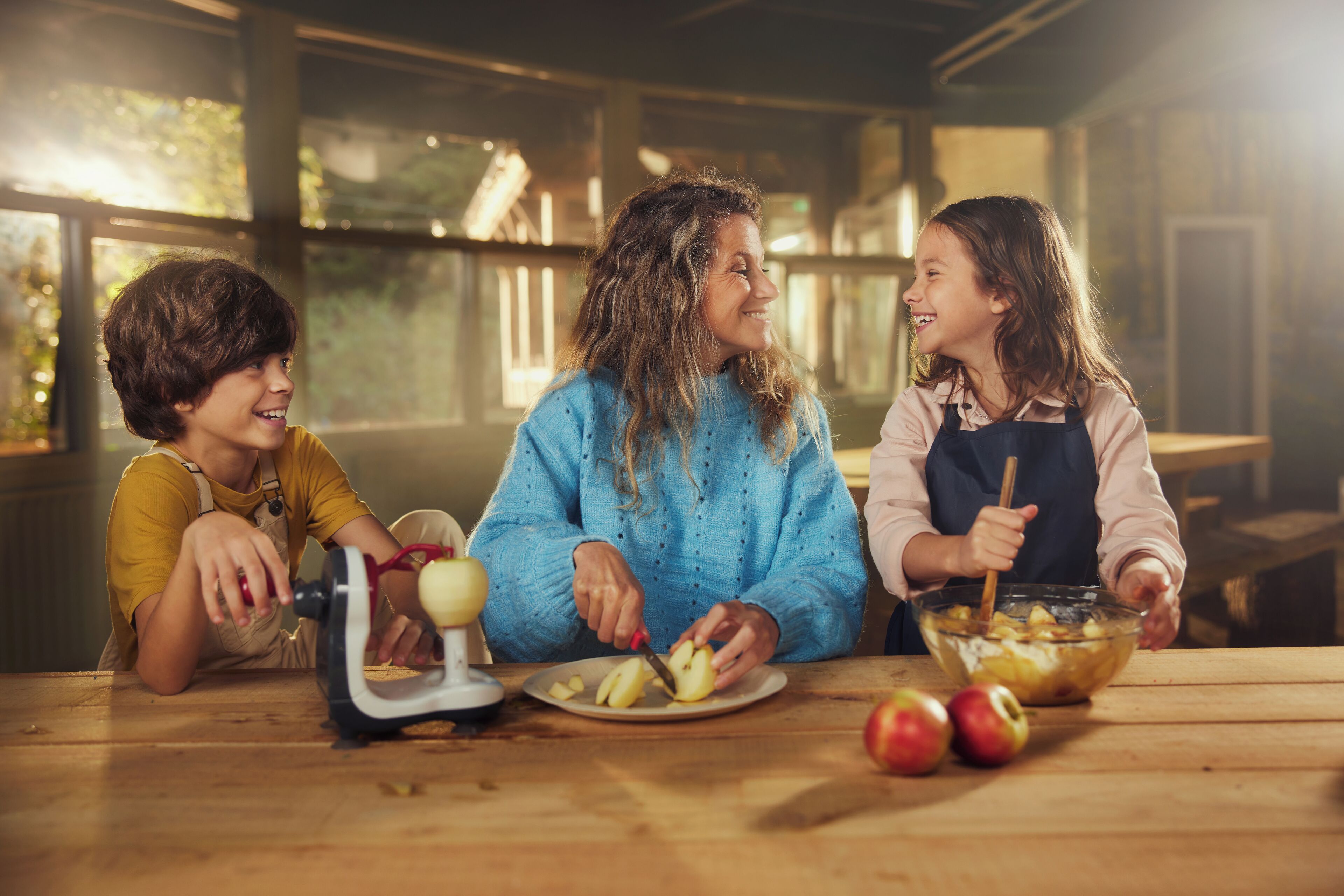 Three people at a wooden table with apples and a food processor.