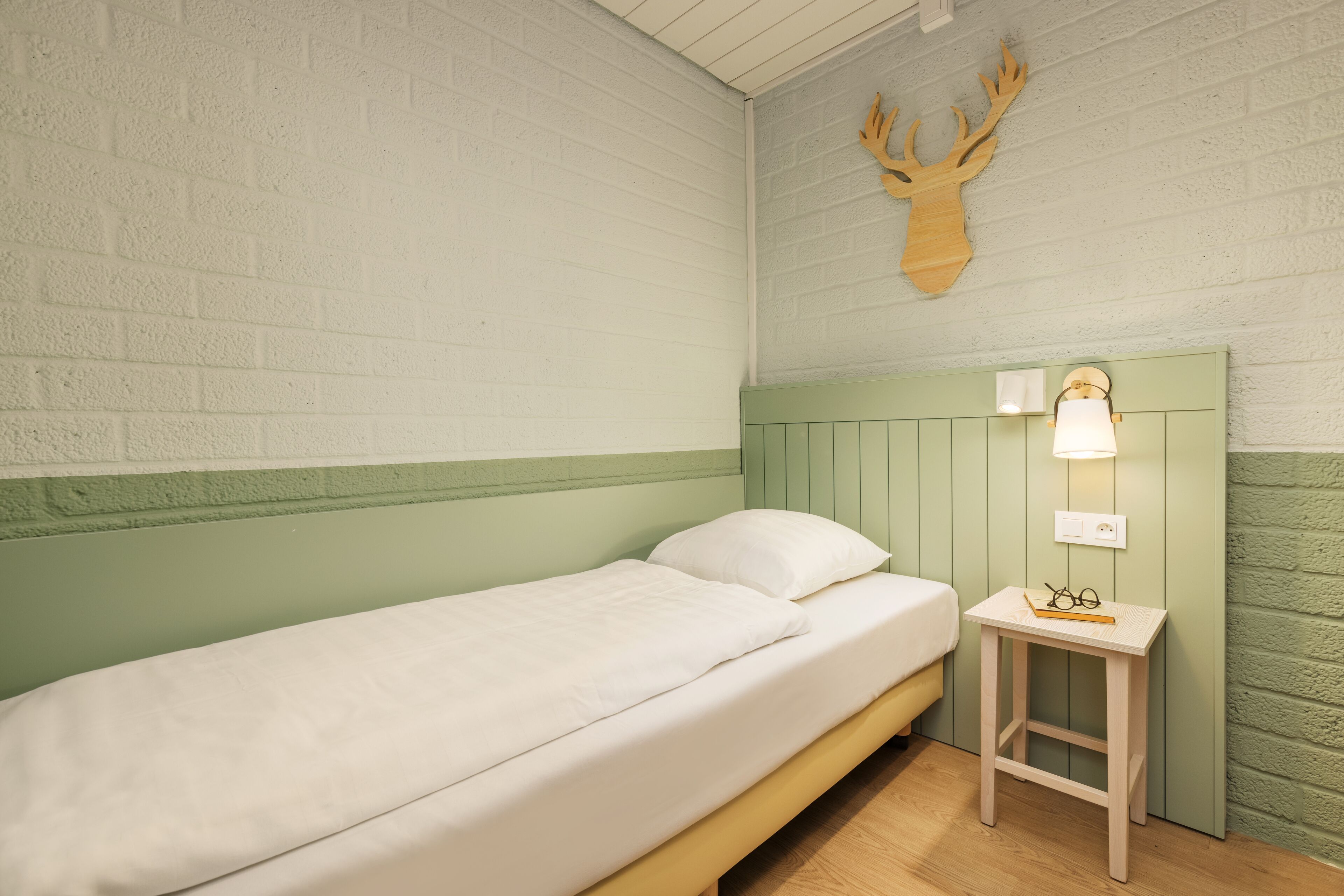 Een enkel bed met een groen hoofdeinde en een klein nachtkastje met een lamp.