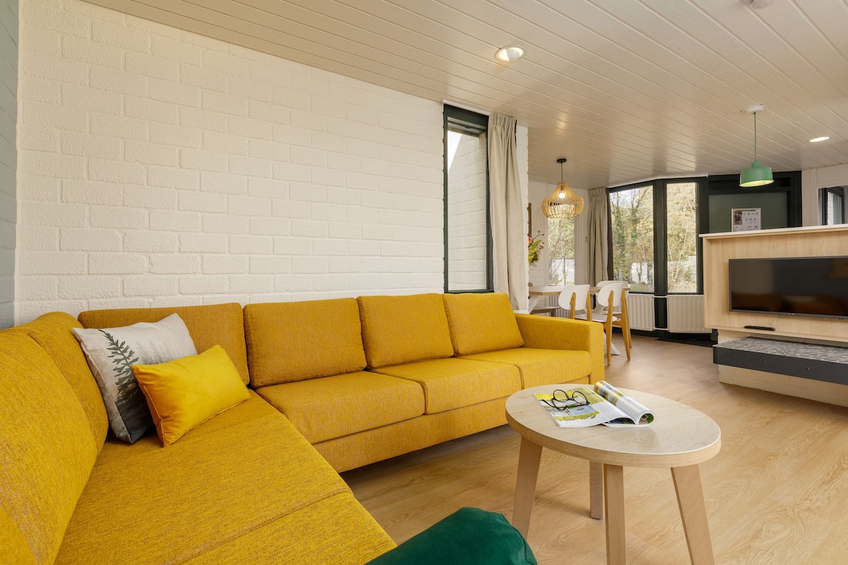 A modern living room with a yellow sofa, a round wooden coffee table, and a TV.