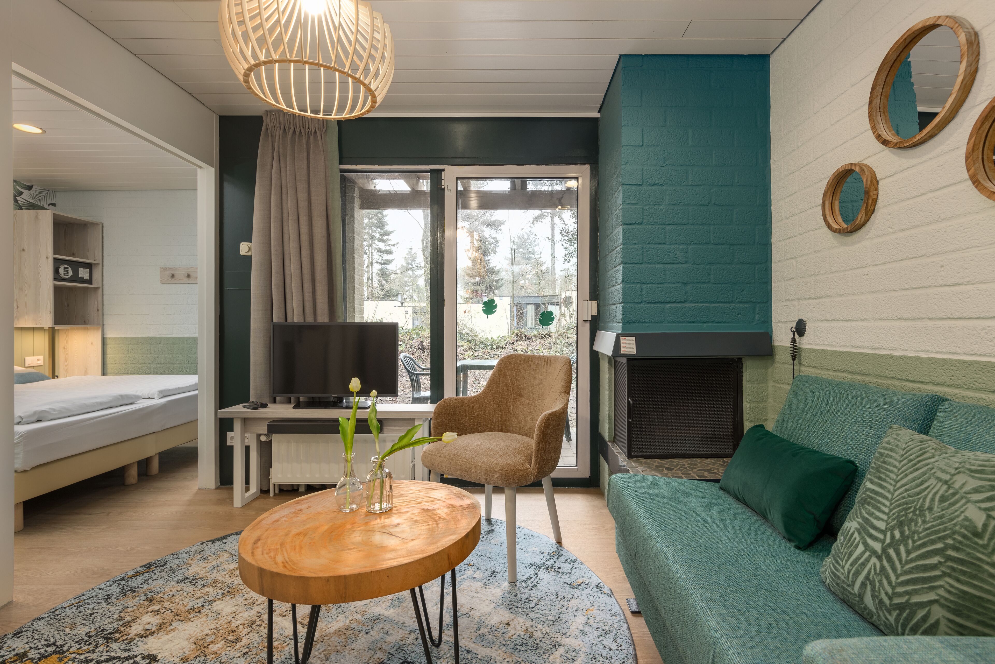 A modern room with a bed, a desk, a chair, a sofa, a fireplace, and a large window.