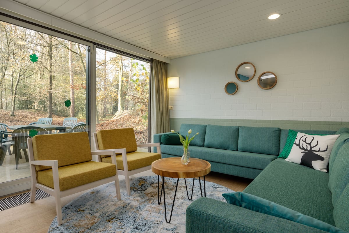 A modern living room with a green sofa, yellow armchairs, and a round wooden coffee table.