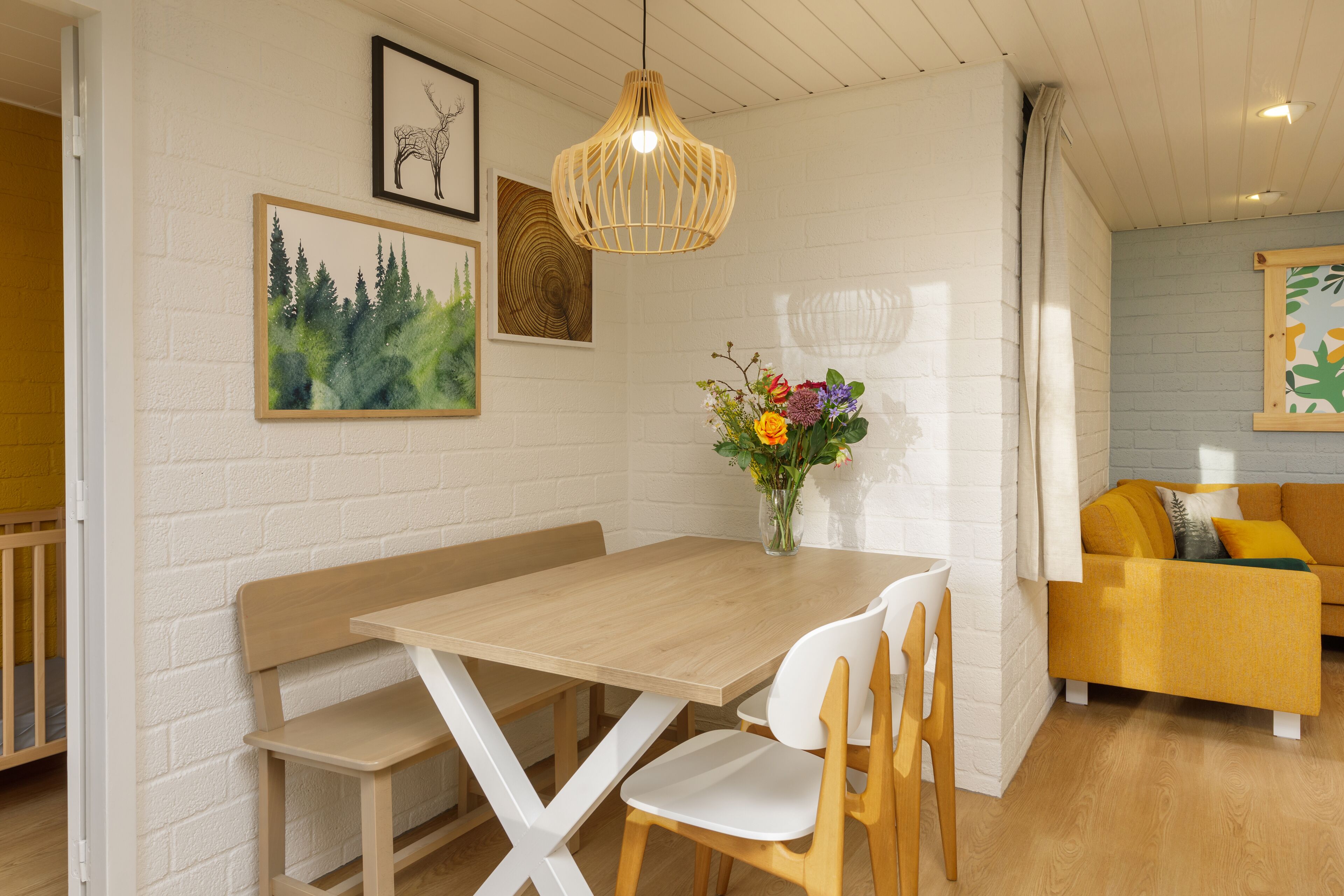 A dining area with a wooden table, white chairs, a bench, and a hanging light fixture.