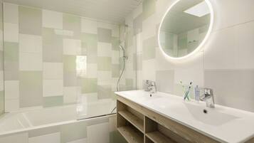 Een moderne badkamer met een glazen douchecabine, een witte wastafel met houten opbergruimte en een ronde spiegel met verlichting.