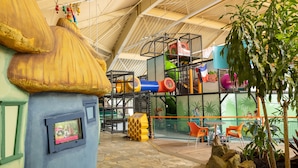Un espace de jeux intérieur comprenant une maison de jeu, des structures d’escalade et un coin salon.