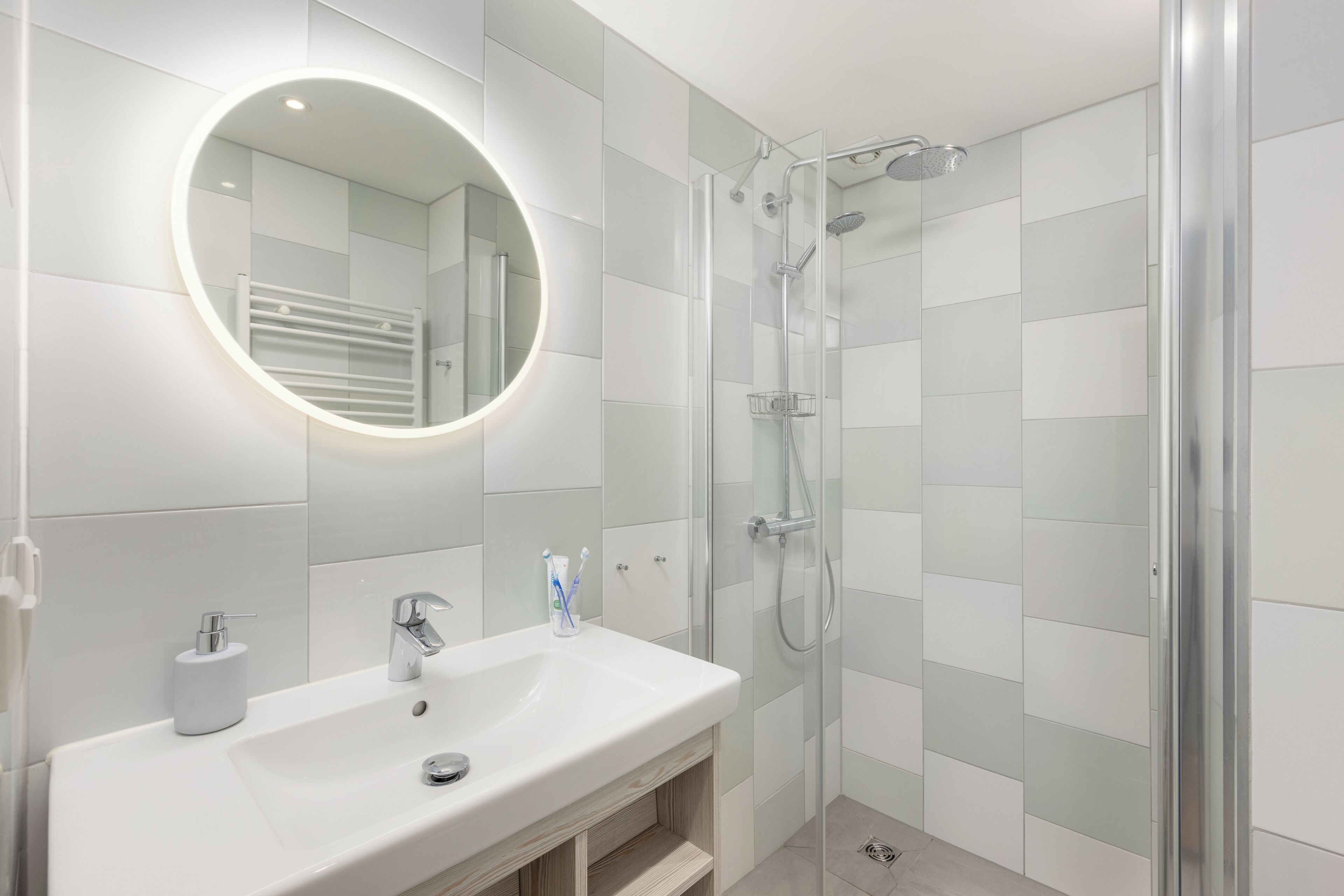 A modern bathroom with a white sink, a round mirror, and a glass-enclosed shower.