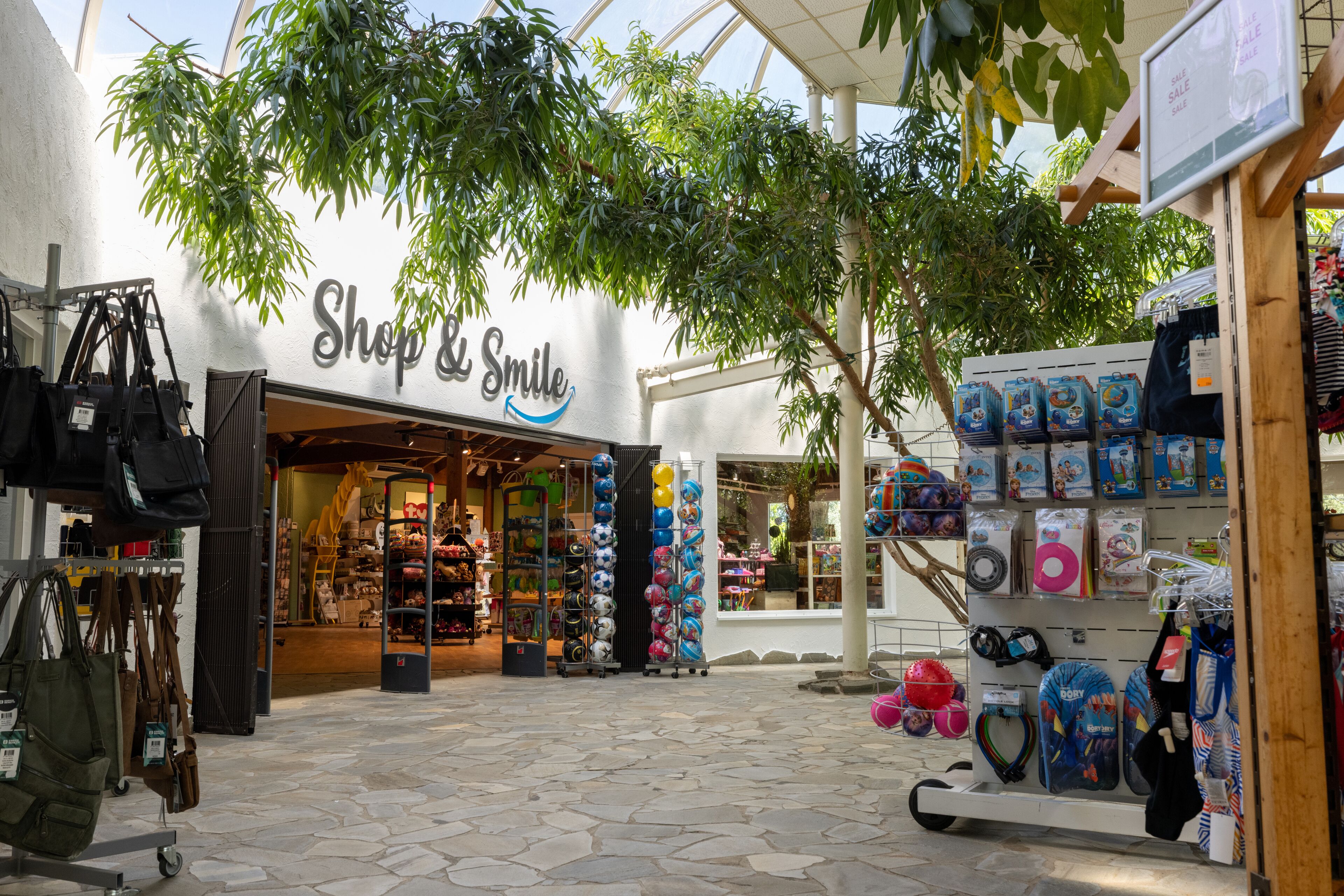 A storefront named 'Shop & Smile' with a variety of items on display, including bags and toys.