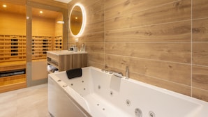 Une salle de bain moderne dotée d’une grande baignoire, de lambris en bois, d’un meuble-lavabo avec miroir et d’une étagère intégrée.