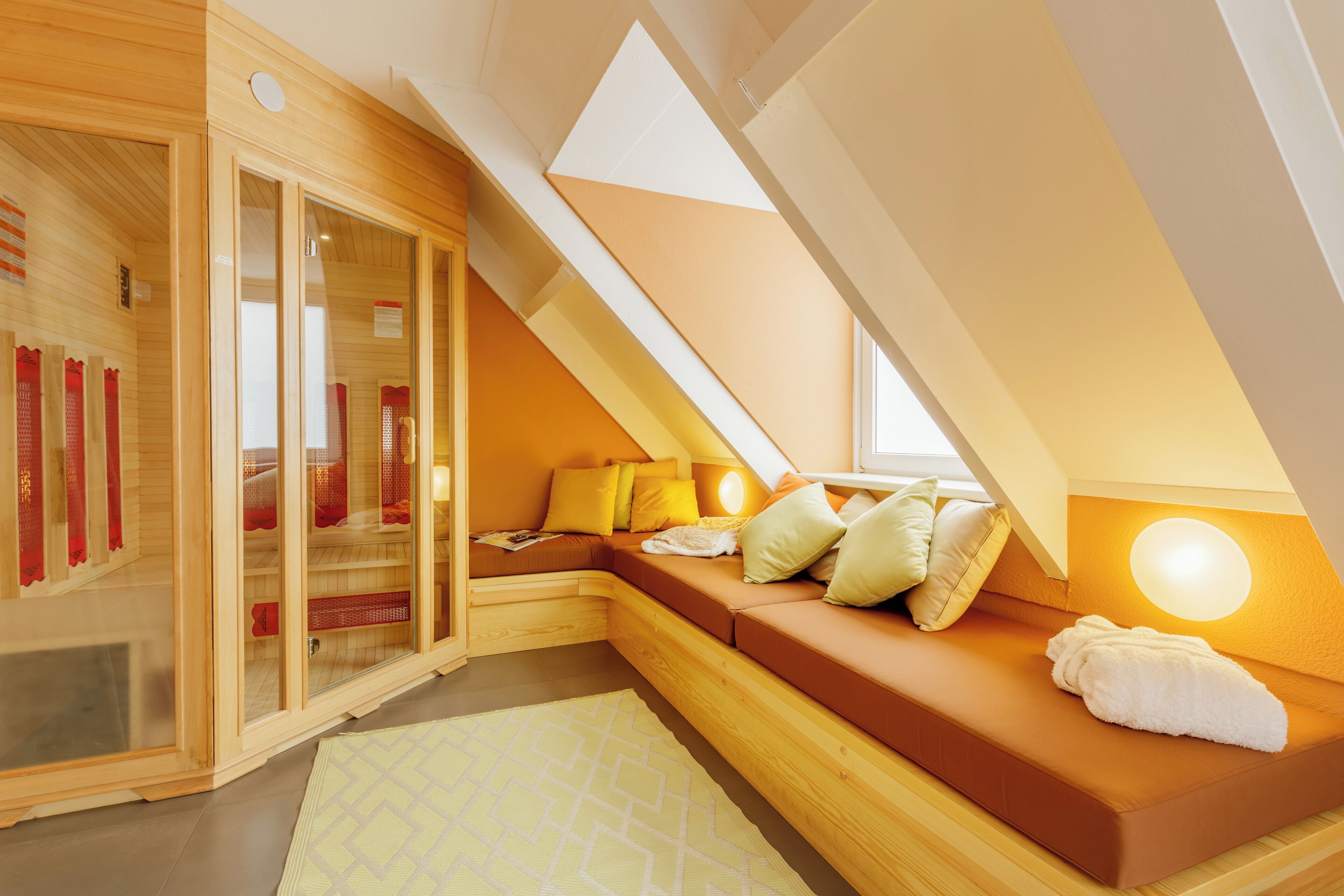Un dormitorio moderno y acogedor con techo inclinado, paredes de madera y un área de descanso integrada con cojines y una manta.