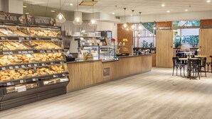 Mostrador de panadería con diversas opciones horneadas, una máquina de café y una zona de estar con mesas y sillas.