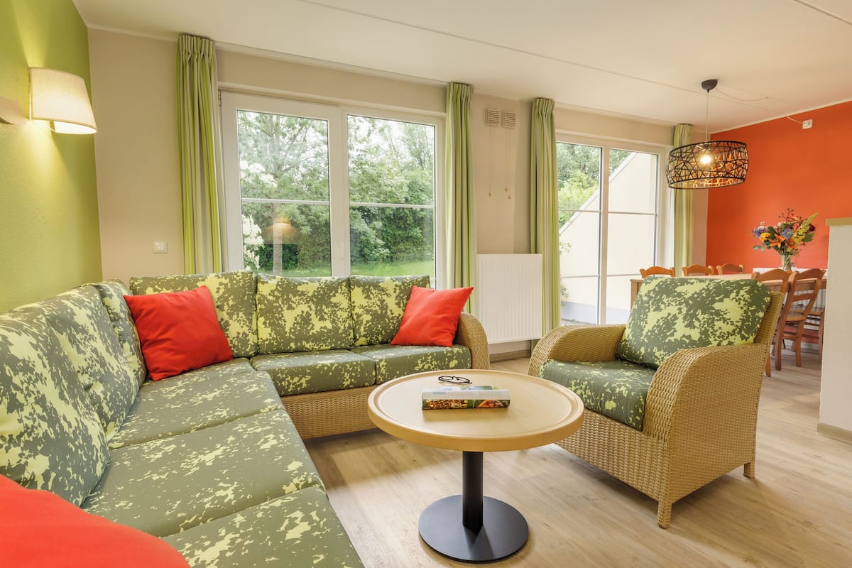 Un salon avec un canapé vert et rouge, une table ronde et un coin repas avec des chaises en osier.