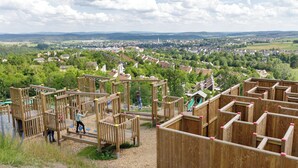 Un parque infantil con estructuras de madera para escalar y una vista de un pueblo al fondo.