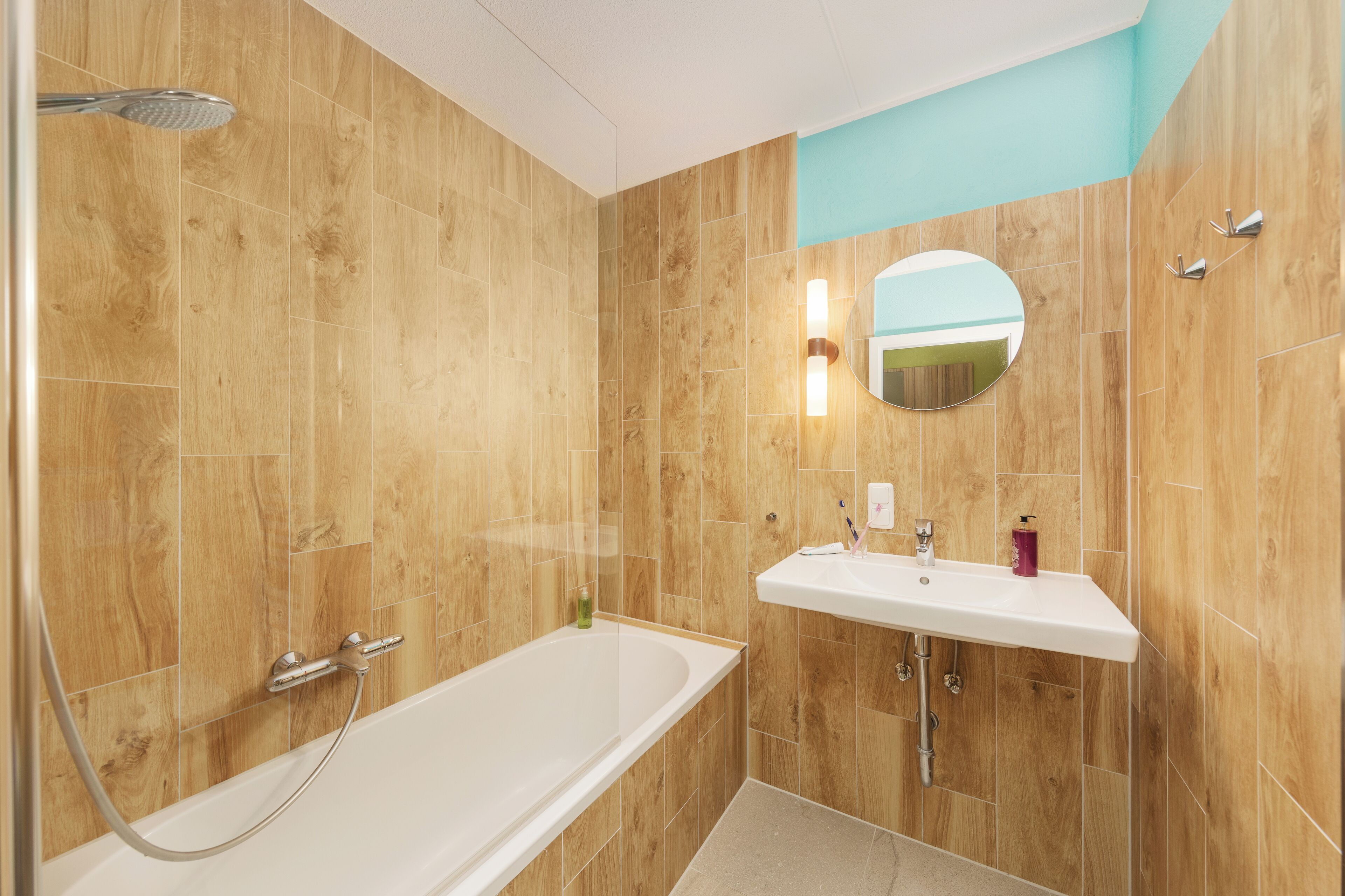 Ein modernes Badezimmer mit einer Holzwand, einer weißen Badewanne, einem Waschbecken mit Spiegel und einer Duschbrause.