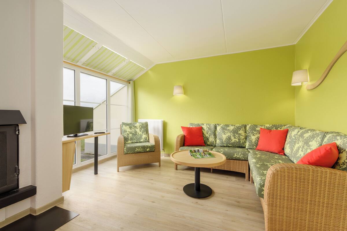 Un salon avec un mur vert, des meubles en osier, une table basse ronde et une cheminée.