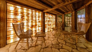 Un área de estar al aire libre con techo, suelo de piedra y mobiliario de madera.