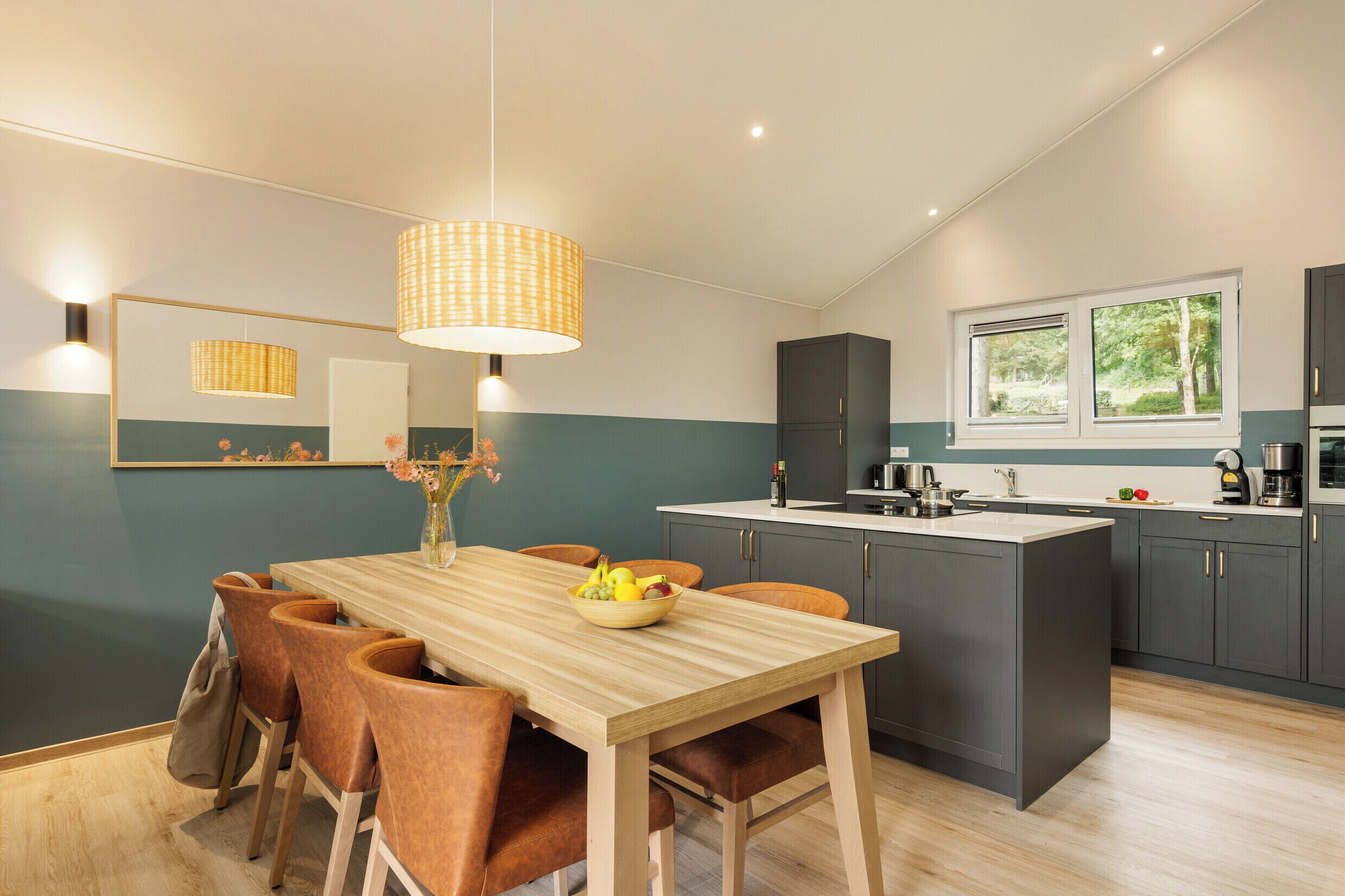 Une cuisine moderne dotée d’un îlot central, de meubles de rangement aux couleurs sombres et d’une fenêtre qui laisse entrer la lumière naturelle.