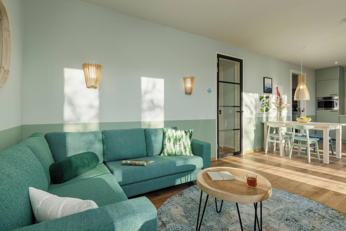 Un salon moderne avec un canapé de couleur turquoise, une table basse en bois et un coin repas comprenant une table et des chaises blanches.