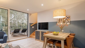 A modern living room with a dining area, a large window, and a staircase leading to an upper level. - Center Parcs Park Eifel (Gunderath)