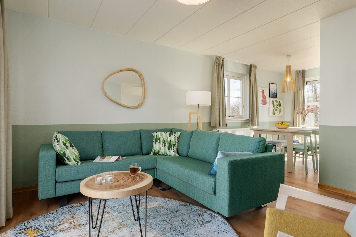 Un salon avec un canapé vert, une table basse ronde en bois et un miroir au mur.