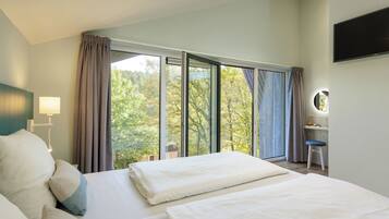 Ein Hotelzimmer mit zwei Betten, einem Schreibtisch mit Stuhl, einem Fernseher und einem großen Fenster mit Vorhängen.