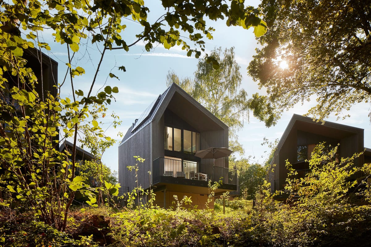 Une maison moderne dotée d’un balcon, entourée d’une végétation luxuriante et d’arbres.