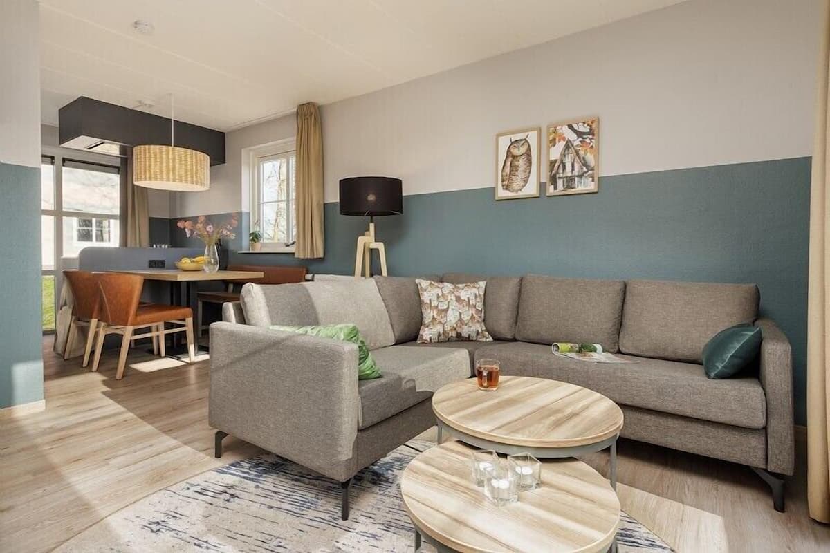 Un salon moderne avec un canapé gris, une table basse ronde et un coin repas comprenant une table et des chaises.