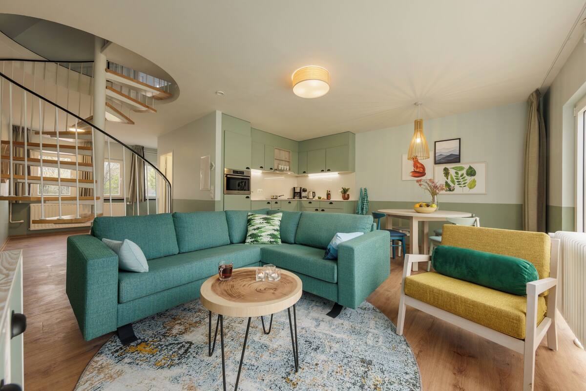 Un salon moderne avec un escalier à volutes, un canapé vert, un fauteuil jaune et une table basse ronde en bois.