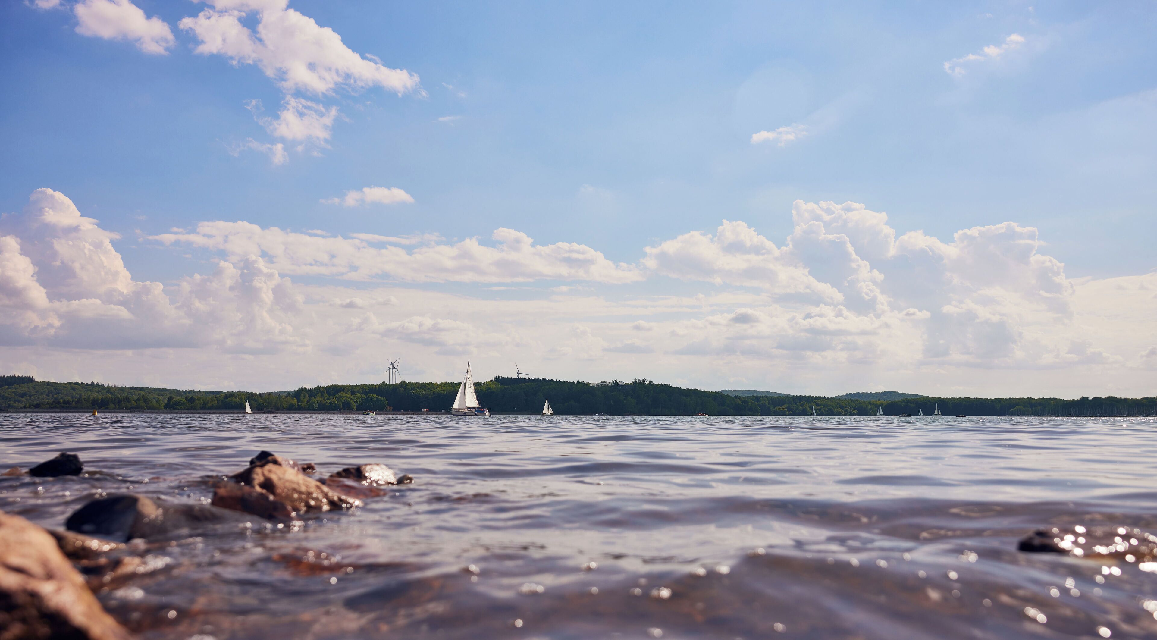 A lake with sailboats and a distant forested hill.