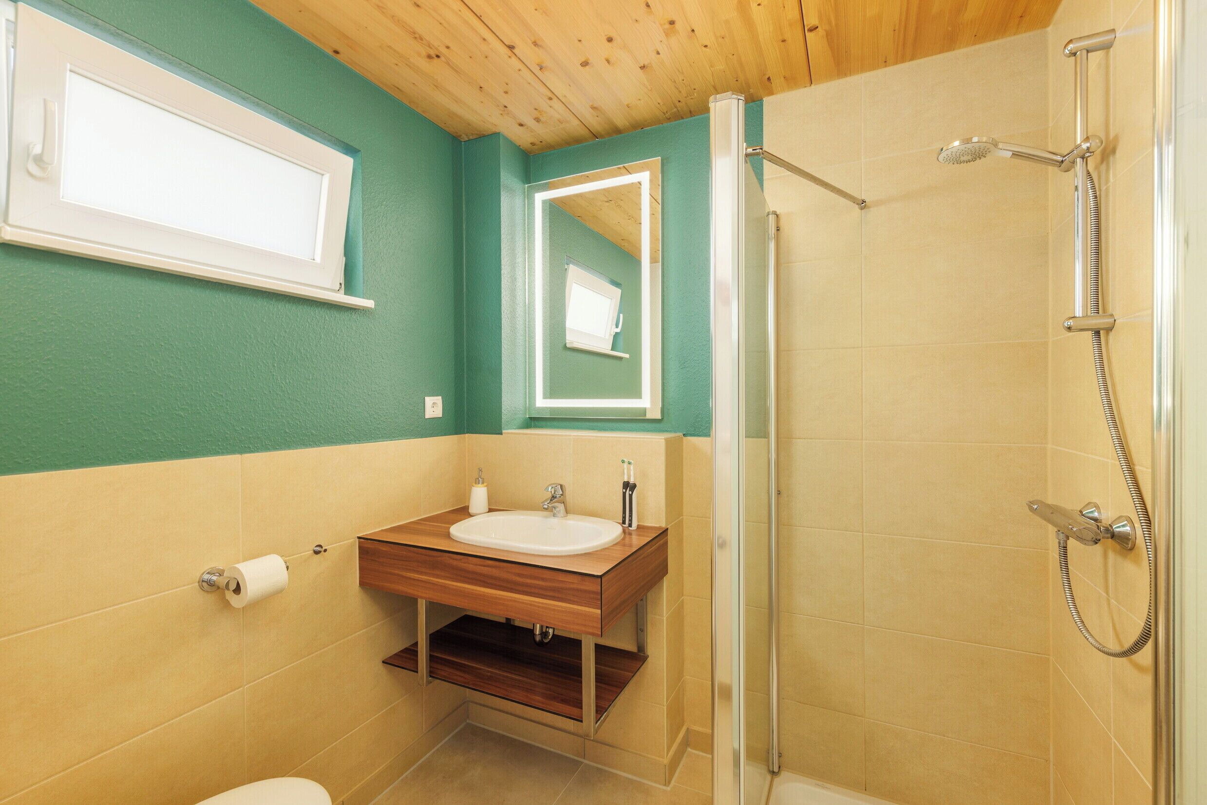 A bathroom with a wooden vanity, a toilet, a shower with a handheld showerhead, and a mirror above the vanity.