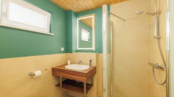 A bathroom with a wooden vanity, a toilet, a shower with a handheld showerhead, and a mirror above the vanity.