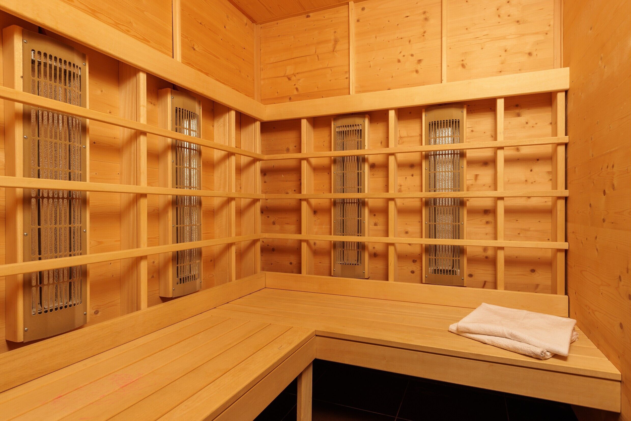 Eine Sauna mit Holzwänden und -bänken, inklusive Lüftungsgitter und einem Handtuch auf einer Bank.