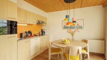 Une cuisine moderne avec des meubles en bois, un four encastré et un coin repas comprenant une table ronde et des chaises jaunes.