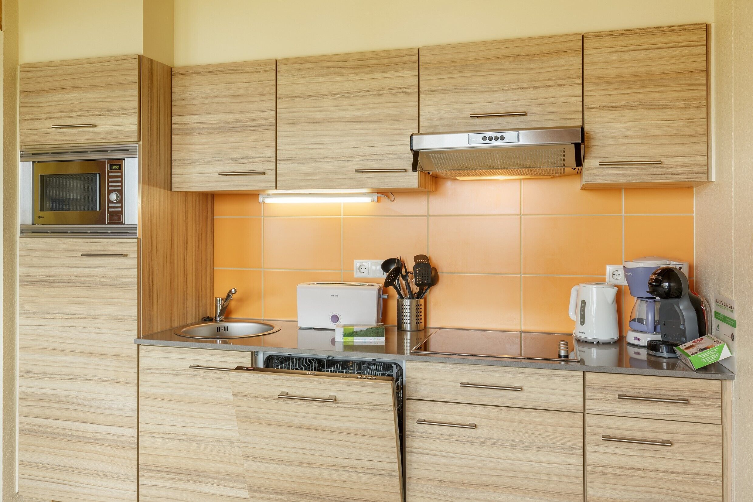 Een keuken met houten kastjes, een magnetron, een broodrooster en een koffiezetapparaat.