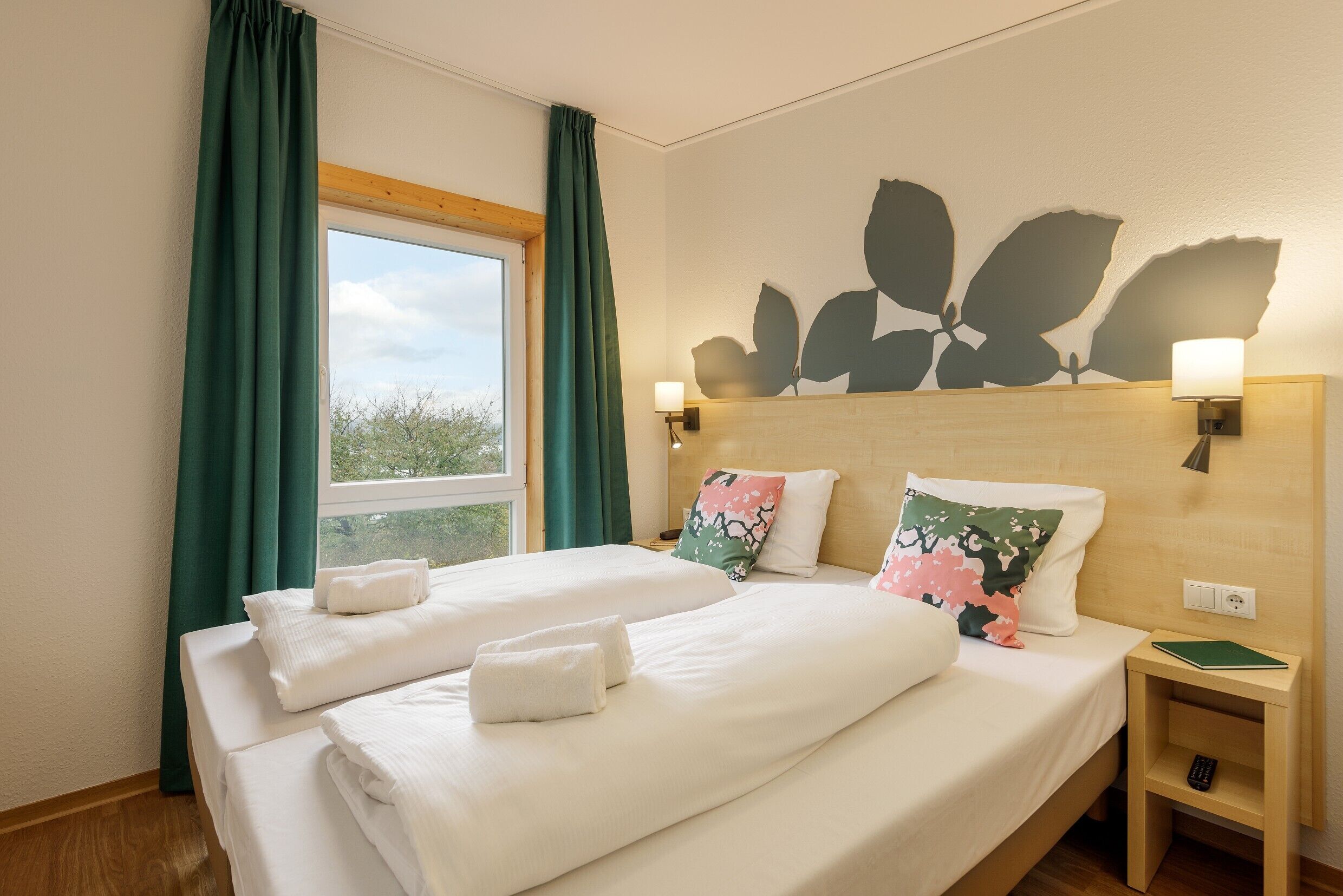 Een tweepersoonsbed met witte lakens, twee kussens, een nachtkastje met een lamp en een afstandsbediening.