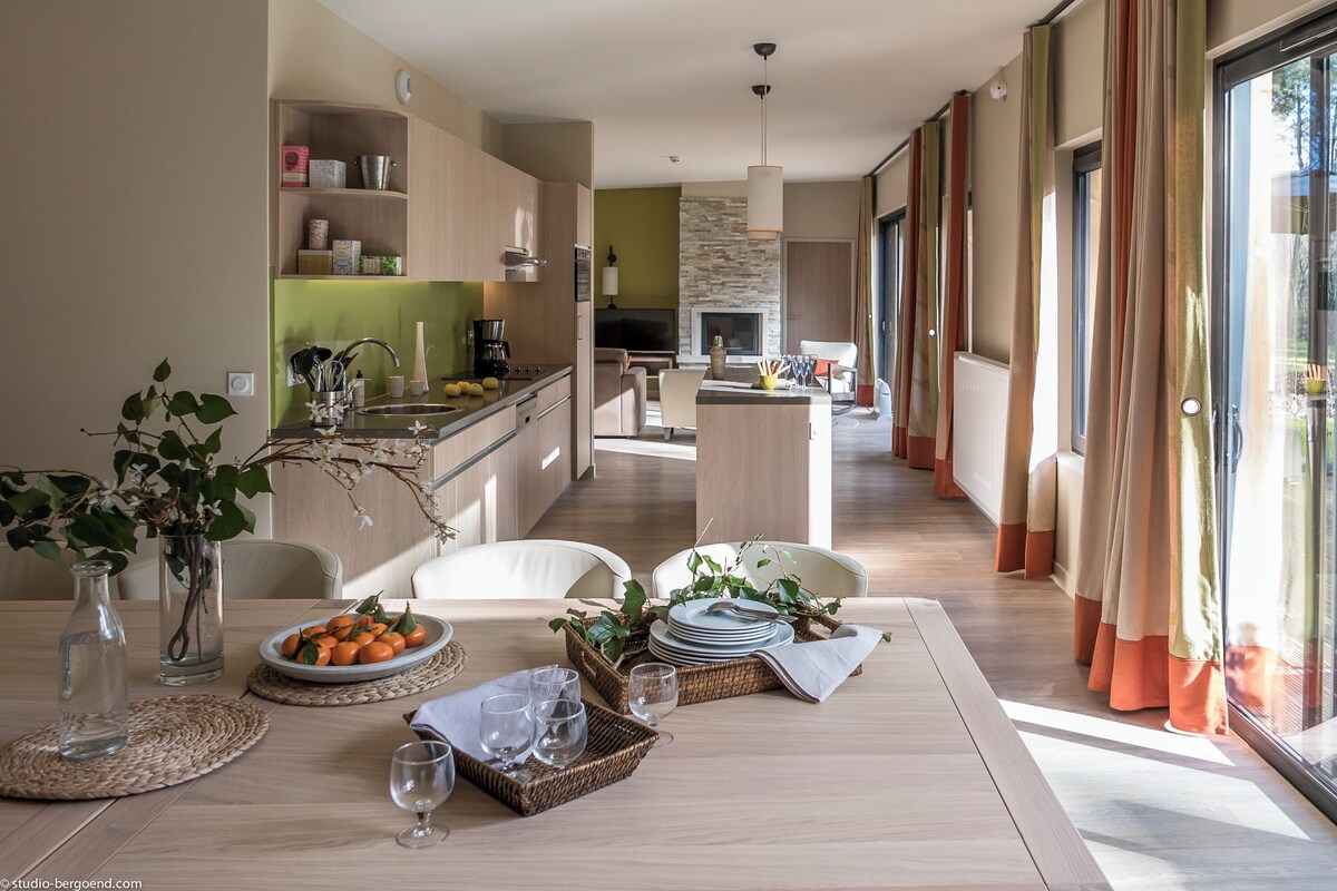 A modern kitchen with a dining area, large windows, and a view of the outdoors.