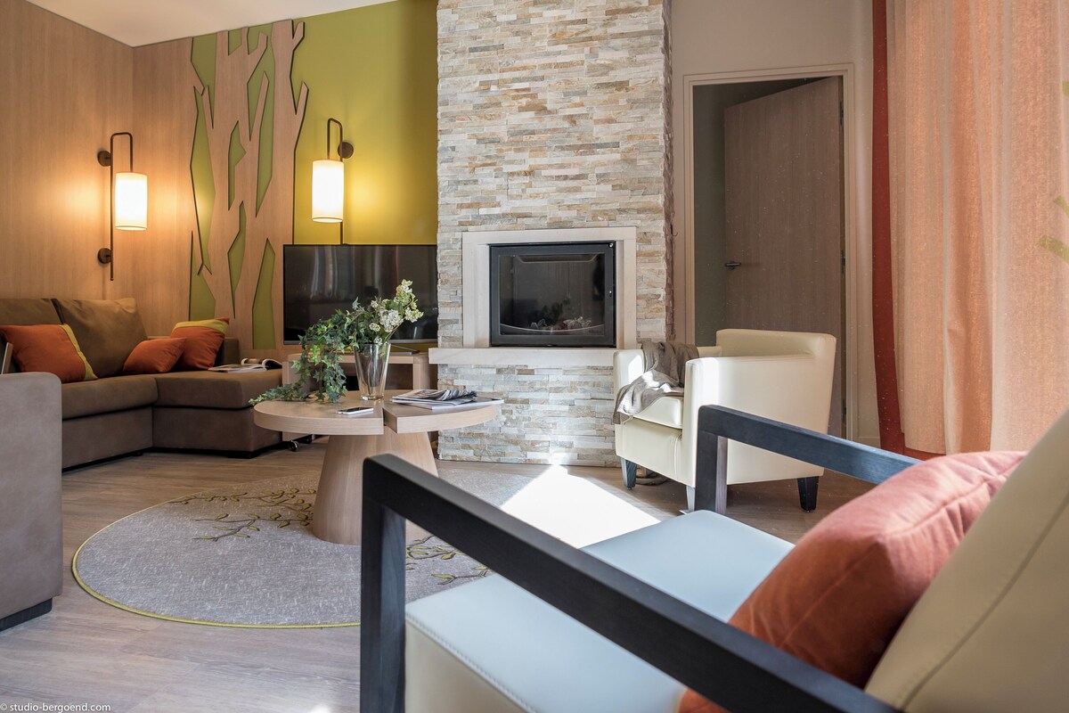 A modern living room with a stone fireplace, a sofa, a coffee table with a vase, and a TV mounted on the wall.