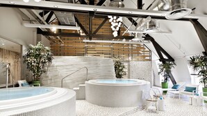 A modern indoor pool area with two hot tubs, seating, and plants. - Center Parcs Le Lac d'Ailette (Chamouille)
