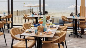 An outdoor dining area with wicker chairs and tables, overlooking a body of water. - Center Parcs Le Lac d'Ailette (Chamouille)