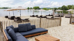 A beachside seating area with a wooden fence, lounge chairs, and umbrellas. - Center Parcs Le Lac d'Ailette (Chamouille)